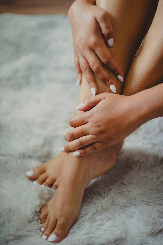 Aesthetic close-up of a woman's manicured hands and legs resting on a soft carpet.